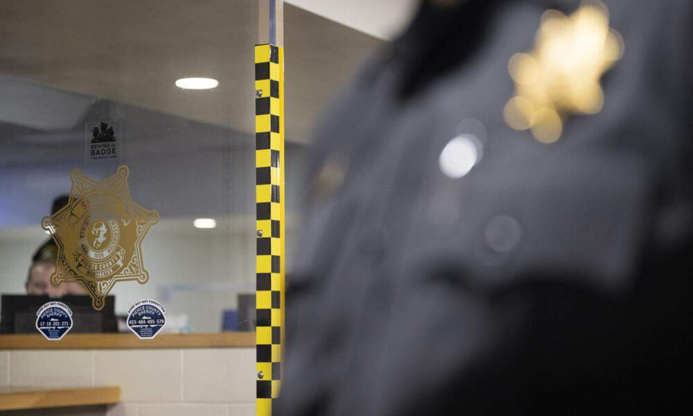 Glass window with a sheriff badge decal and security stickers; a blurred police officer is visible on the right.