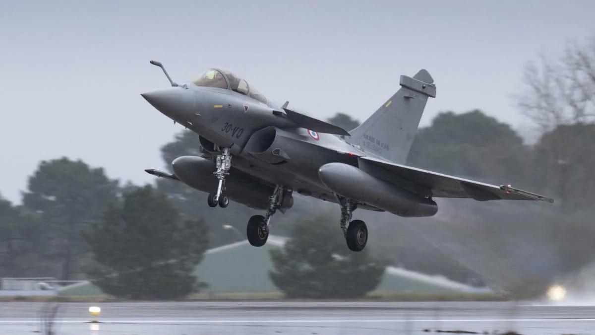 Two-seat military fighter jet lifting off the wet runway in overcast weather, gear still extended.