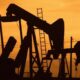 Silhouetted oil pumpjacks against an orange sunset sky.