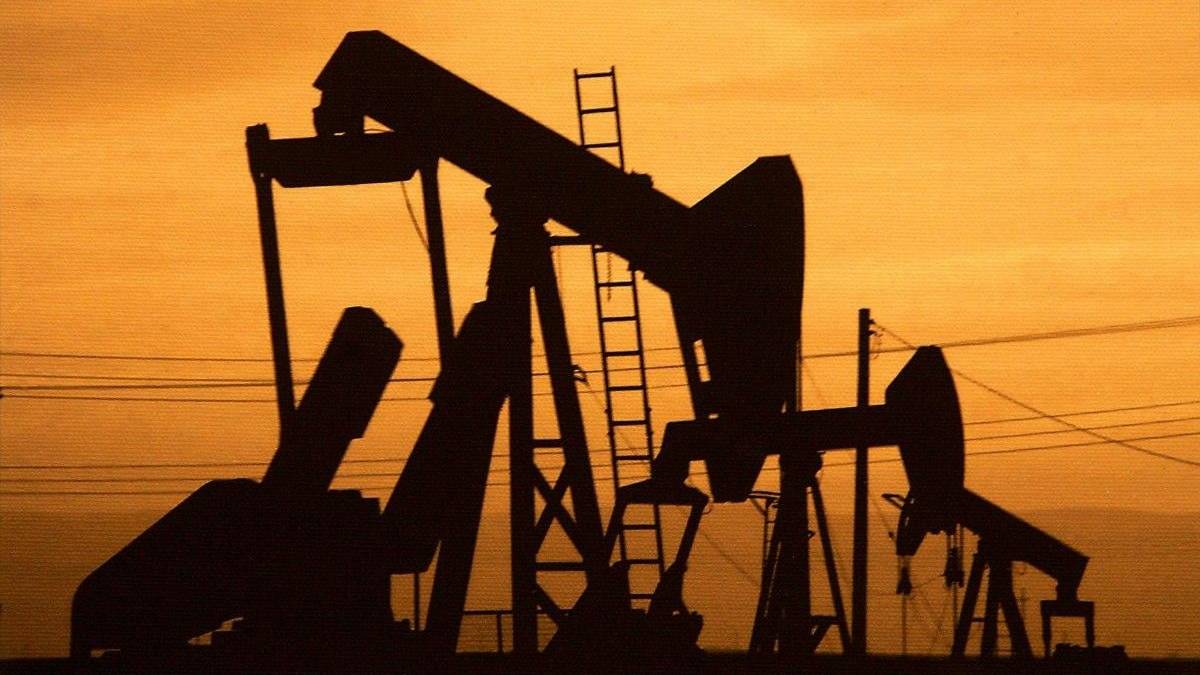 Silhouetted oil pumpjacks against an orange sunset sky.