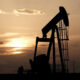 Silhouetted oil pumpjack against an orange sunset on a flat horizon