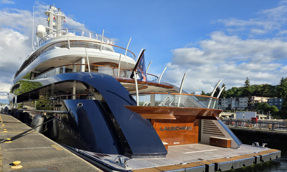 Large luxury yacht docked at a marina under a blue sky, name Launchpad visible on the stern area