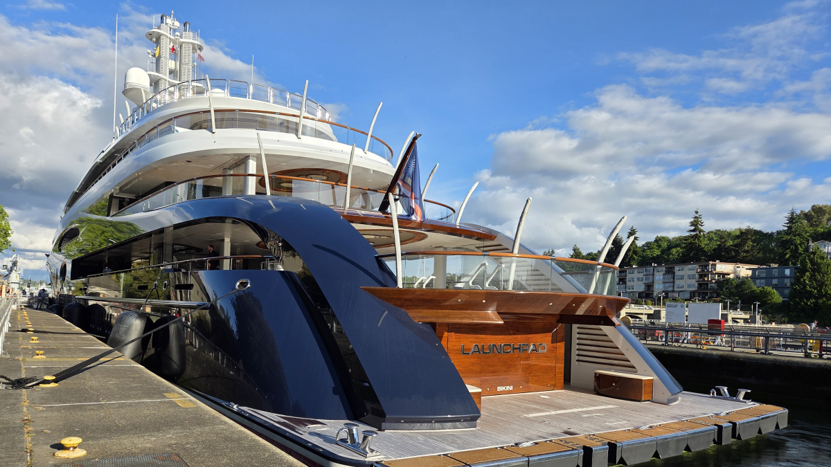 Large luxury yacht docked at a marina under a blue sky, name Launchpad visible on the stern area