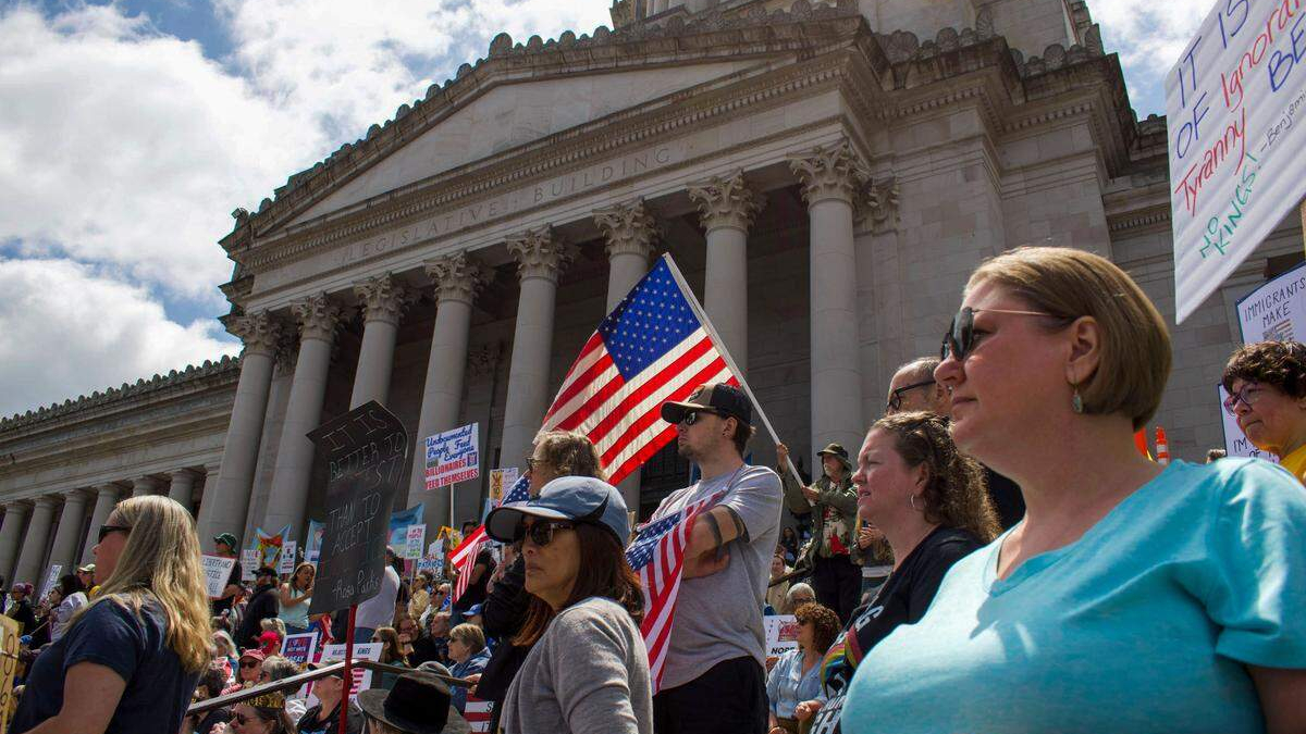 Protesters outside a large neoclassical government building, some holding signs and American flags.