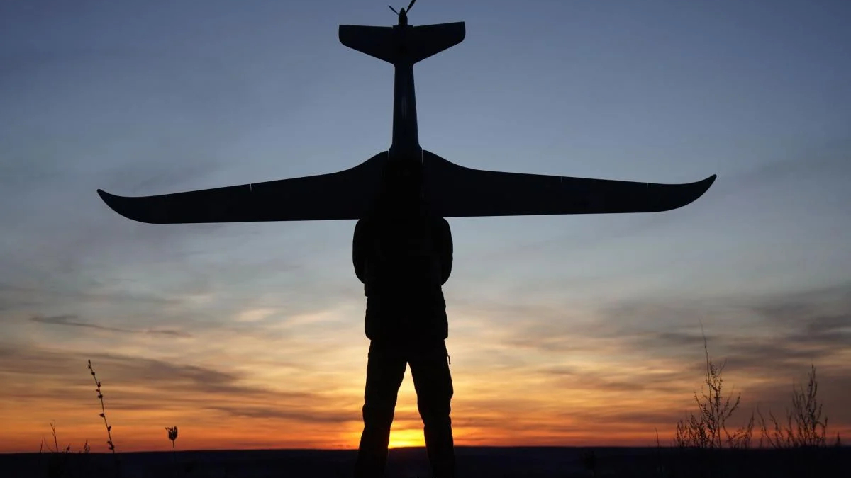 silhouette of a person lifting a small airplane glider above their head at sunset, orange and blue sky in the background.
