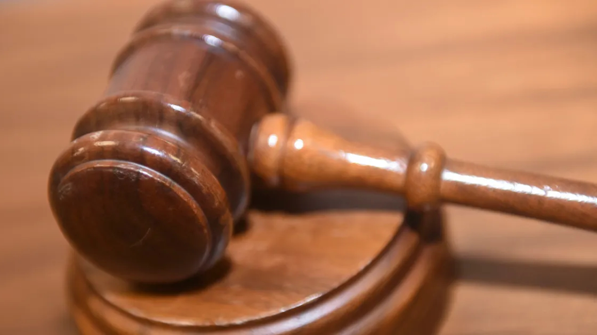 Wooden judge's gavel resting on a sound block on a courtroom table.