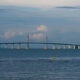 Long bridge spanning a calm sea with a central cable-stayed section and a small island in the distance.
