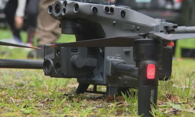 Close-up of a gray quadcopter drone on grass, revealing its multi-lens camera and landing gear in the foreground.
