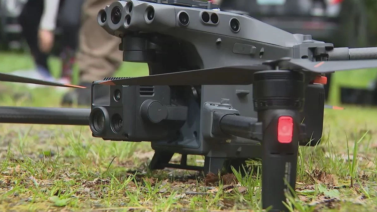 Close-up of a gray quadcopter drone on grass, revealing its multi-lens camera and landing gear in the foreground.