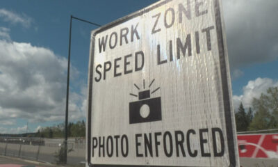 Large road work zone sign stating 'Work Zone Speed Limit' with 'Photo Enforced' at a construction site under a blue sky.