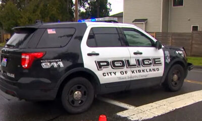Black-and-white City of Kirkland police SUV with blue emergency lights, parked on a street; side reads POLICE, CITY OF KIRKLAND, and a motto below.
