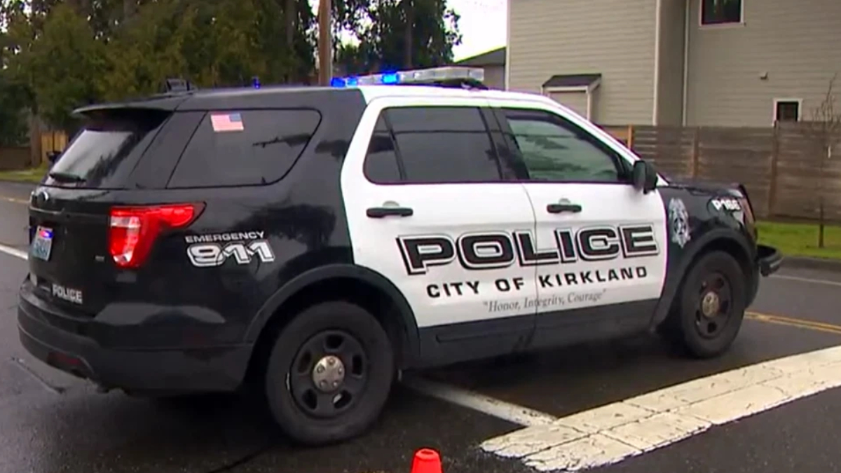 Black-and-white City of Kirkland police SUV with blue emergency lights, parked on a street; side reads POLICE, CITY OF KIRKLAND, and a motto below.