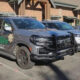Two gray sheriff patrol SUVs with heavy front bumpers parked in a lot beside a brick building.