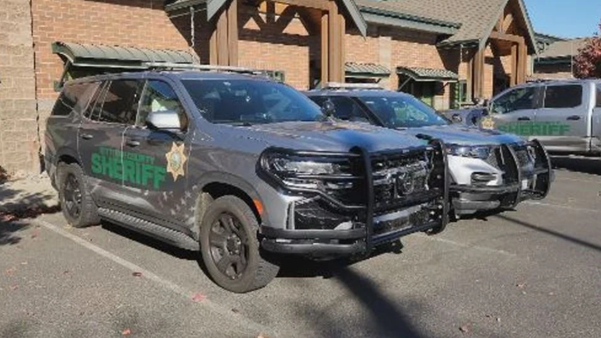 Two gray sheriff patrol SUVs with heavy front bumpers parked in a lot beside a brick building.