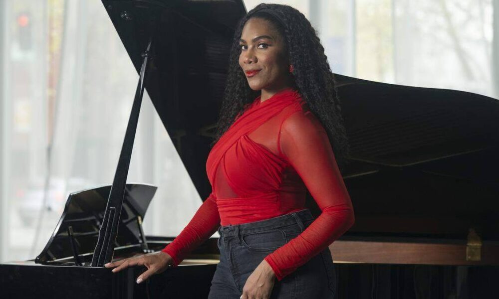 Woman in a red top posing beside a grand piano in a bright studio setting