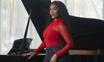 Woman in a red top posing beside a grand piano in a bright studio setting