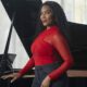 Woman in a red top posing beside a grand piano in a bright studio setting