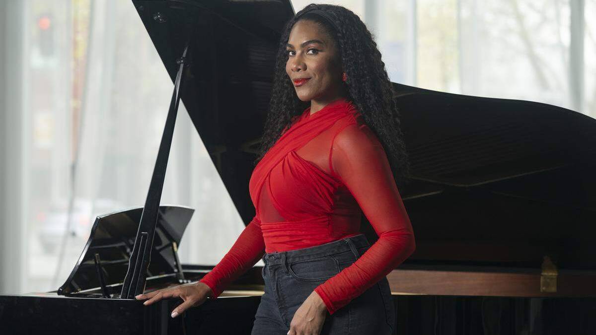 Woman in a red top posing beside a grand piano in a bright studio setting