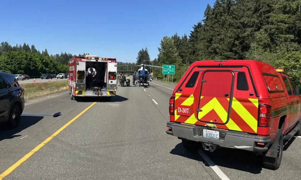 Emergency responders on a highway with a backup of vehicles, a red fire/ambulance truck, and a helicopter on the road nearby.