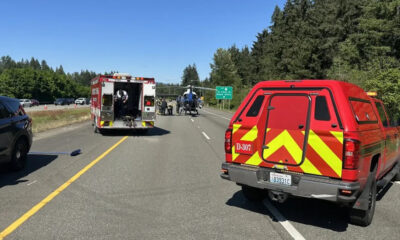 Emergency responders on a highway with a backup of vehicles, a red fire/ambulance truck, and a helicopter on the road nearby.