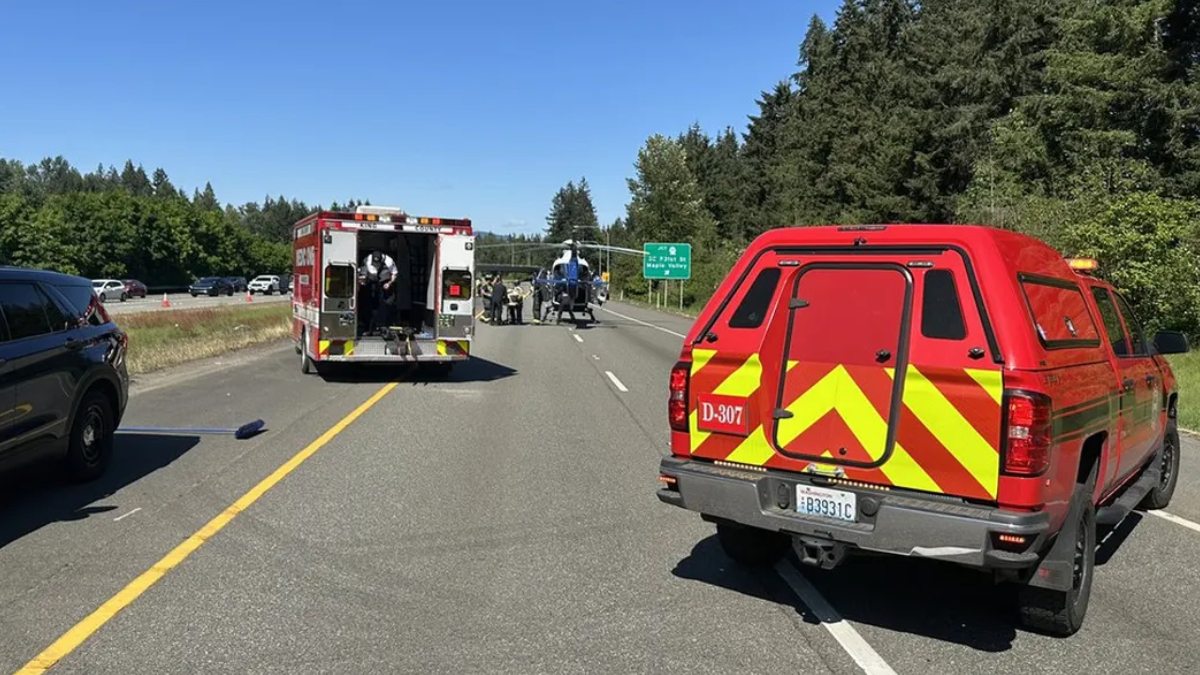 Emergency responders on a highway with a backup of vehicles, a red fire/ambulance truck, and a helicopter on the road nearby.