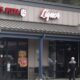 Front of a strip-mall pizza shop with Figaro's Pizza and Liquor signs; an elderly man exits carrying a bag.