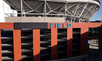 Exterior view of a stadium with an orange facade, multi-level parking, and a blue SIGN reading FIELD on top of the building.