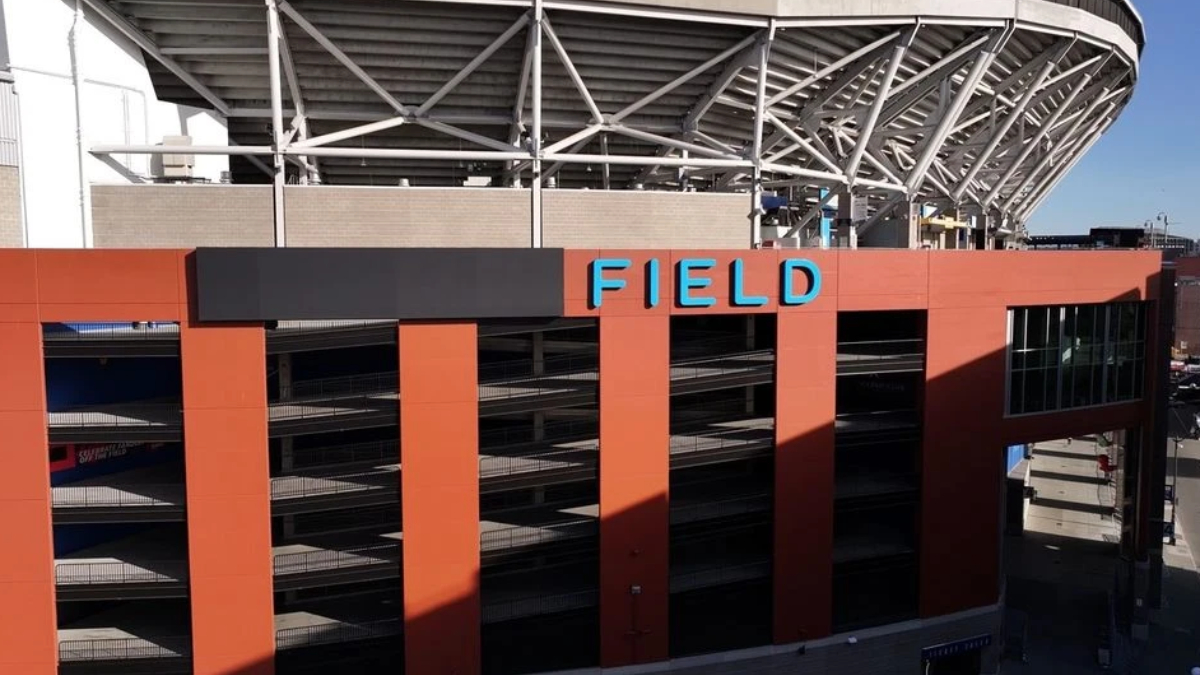 Exterior view of a stadium with an orange facade, multi-level parking, and a blue SIGN reading FIELD on top of the building.
