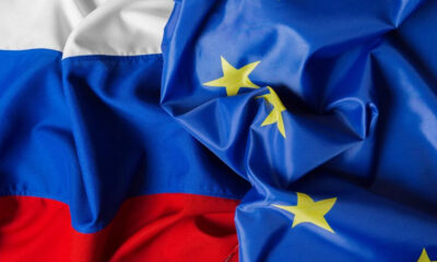 Russian flag partially draped over the European Union flag with yellow stars on blue field and red stripe visible at the bottom left