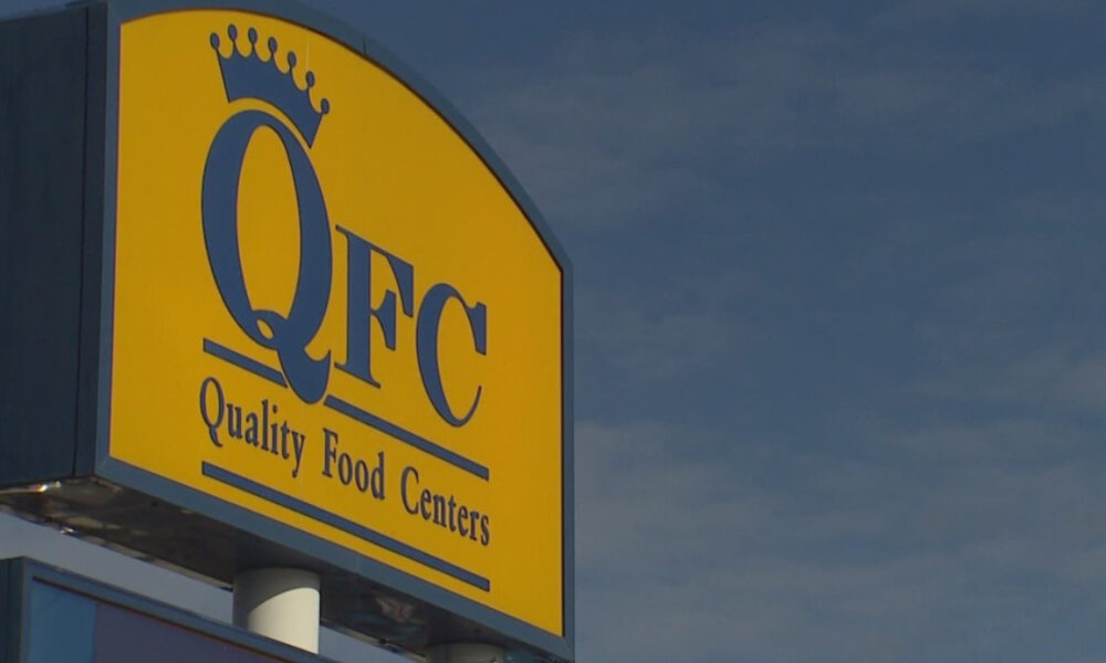 QFC store sign on a yellow panel with a crown logo and the words 'Quality Food Centers' against a blue sky.