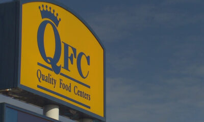 QFC store sign on a yellow panel with a crown logo and the words 'Quality Food Centers' against a blue sky.