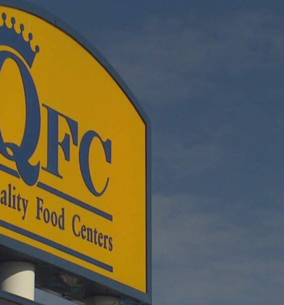 QFC store sign on a yellow panel with a crown logo and the words 'Quality Food Centers' against a blue sky.