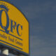 QFC store sign on a yellow panel with a crown logo and the words 'Quality Food Centers' against a blue sky.