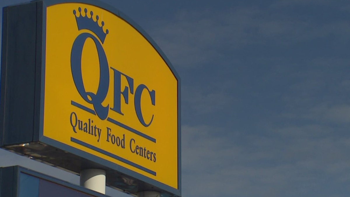 QFC store sign on a yellow panel with a crown logo and the words 'Quality Food Centers' against a blue sky.