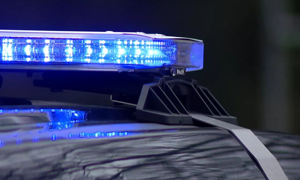 Blue flashing emergency lights on the roof of a police car, reflecting off the hood.