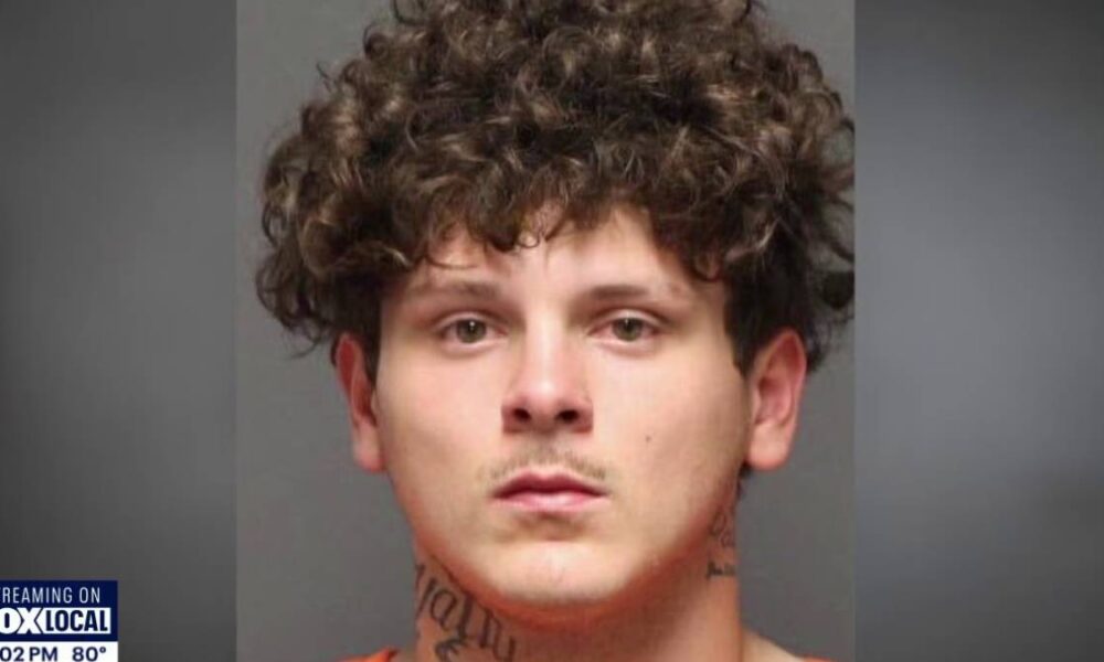 Mugshot of a young man with curly brown hair and neck tattoos, neutral expression