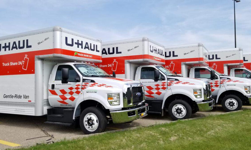 Row of white U-Haul moving trucks with red checkered decals parked on a lot.