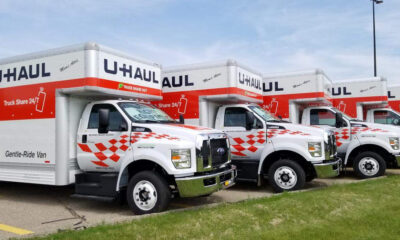 Row of white U-Haul moving trucks with red checkered decals parked on a lot.