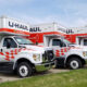 Row of white U-Haul moving trucks with red checkered decals parked on a lot.