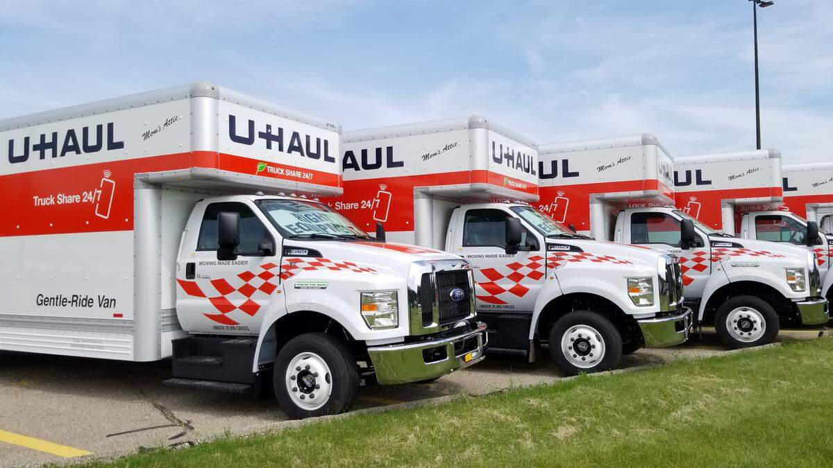 Row of white U-Haul moving trucks with red checkered decals parked on a lot.