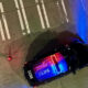 Top-down view of a police car with red and blue lights on, seen from above on a street with orange cones; text POLICE/STATE visible on the roof.