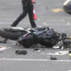 Motorcycle lying on its side in a road crash with scattered debris and a patrol car cone in the background.