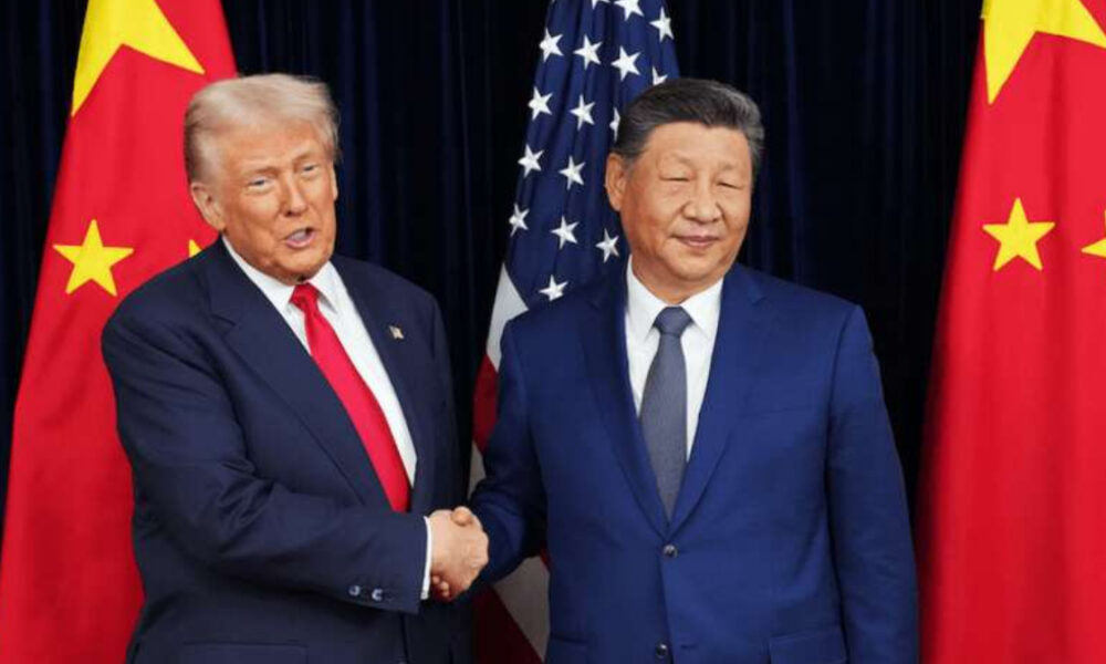 Two men in suits shake hands in front of US and China flags behind them.