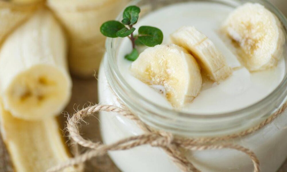Creamy banana smoothie in a mason jar, topped with banana slices and a small green sprig.