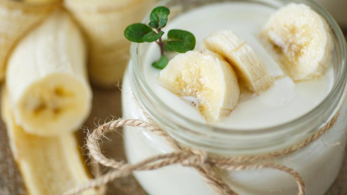Creamy banana smoothie in a mason jar, topped with banana slices and a small green sprig.