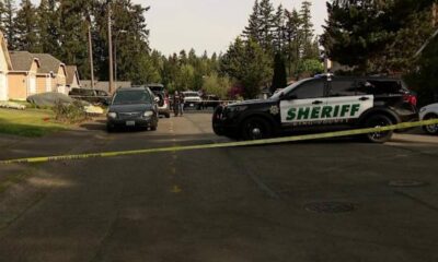 Sheriff patrol SUV blocks a residential street with yellow tape as investigators work in the background.