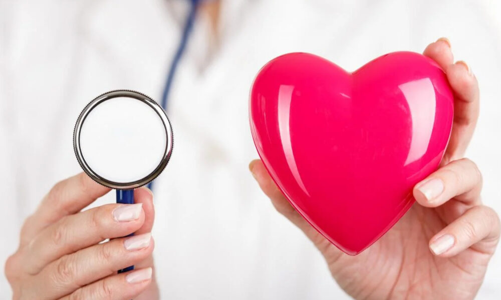 Doctor holding a stethoscope and a glossy pink heart, symbolizing heart health care or cardiology.