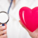 Doctor holding a stethoscope and a glossy pink heart, symbolizing heart health care or cardiology.
