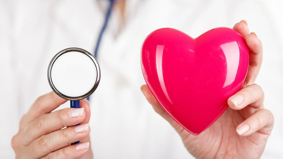 Doctor holding a stethoscope and a glossy pink heart, symbolizing heart health care or cardiology.