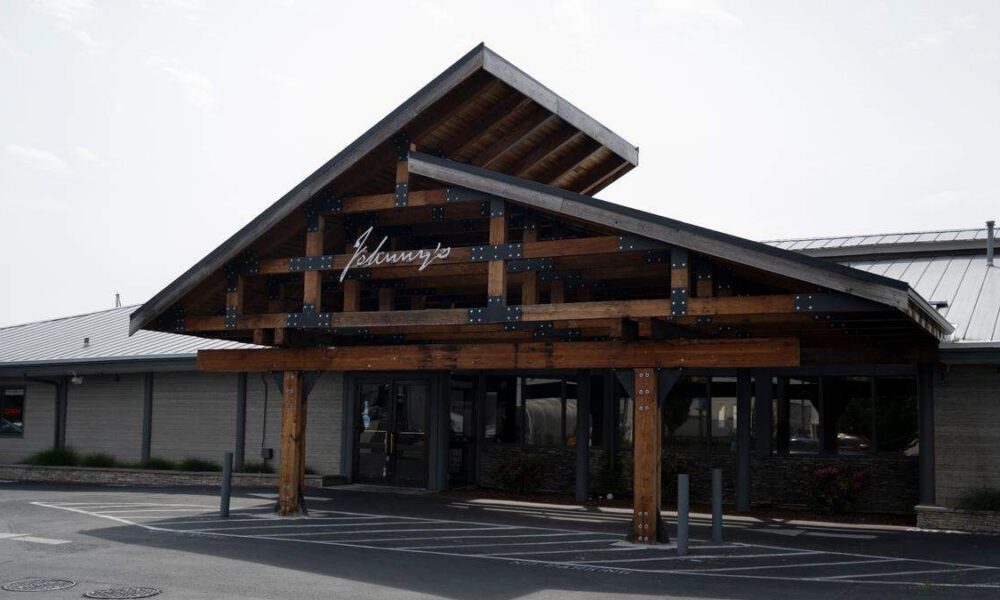 Wooden entrance canopy with metal brackets over a storefront, featuring glass doors beneath.